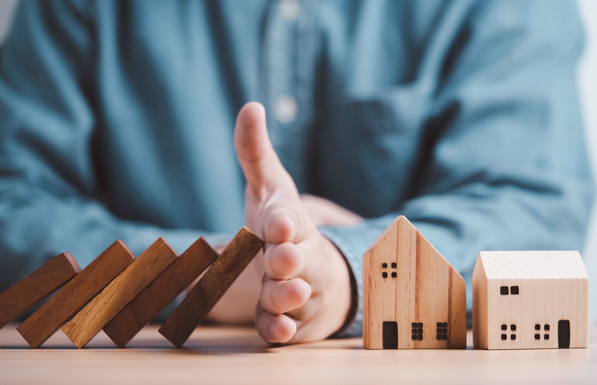 Businessman hand protect and stop wooden house from domino falling wooden bar for risk management and analysis of real estate concept.